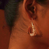 Close profile of Maré natural pearl statement earring in 24k gold worn on model in warm editorial light.