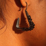 Close-up of Maré black rhodium statement earring with natural spinel beads worn close to ear on model.