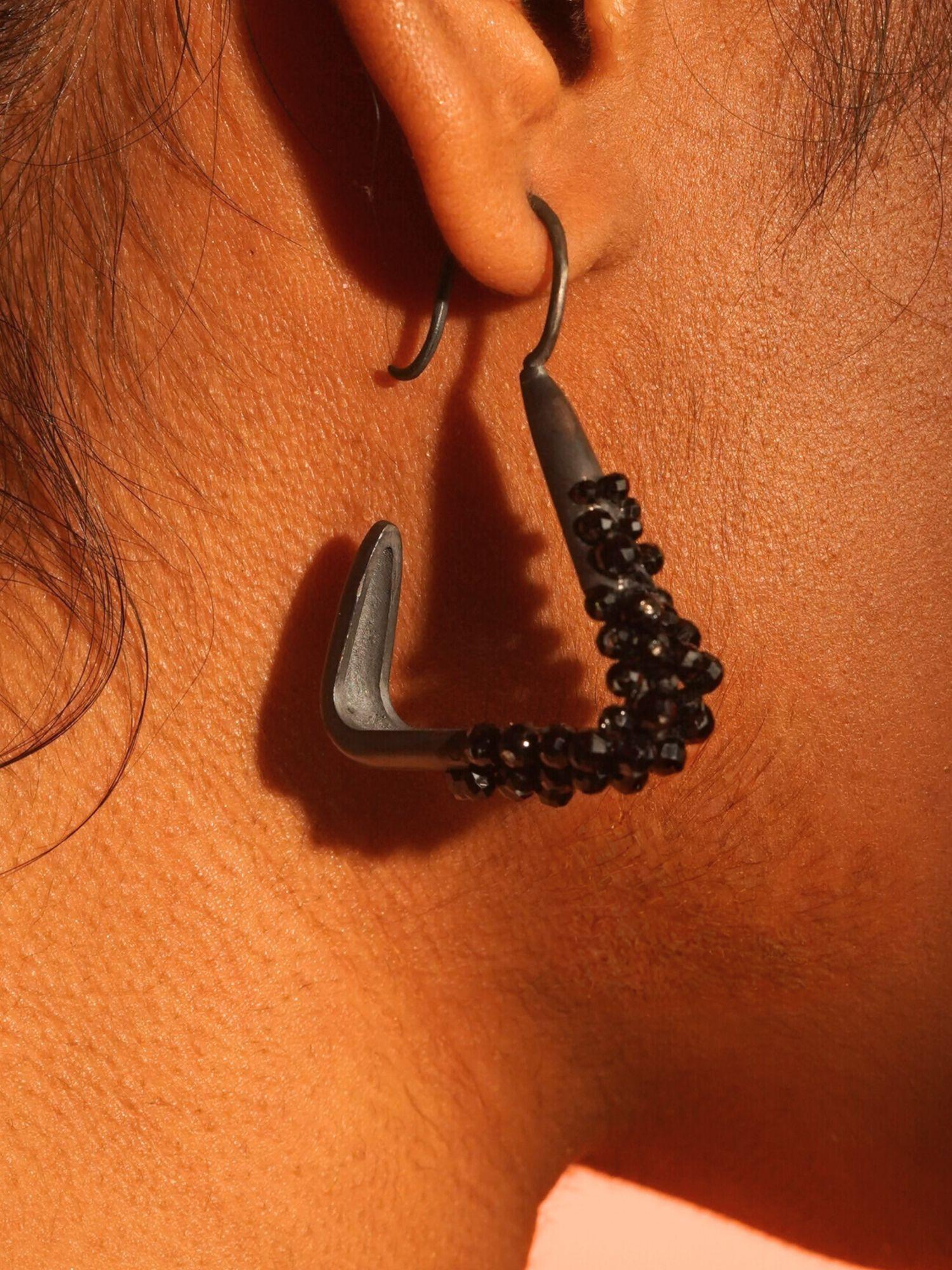 Close-up of Maré black rhodium statement earring with natural spinel beads worn close to ear on model.