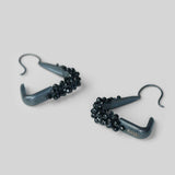 Angled product shot of Maré spinel hanger earrings in black rhodium showing triangular silhouette and bead detail.