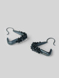 Angled product shot of Maré spinel hanger earrings in black rhodium showing triangular silhouette and bead detail.