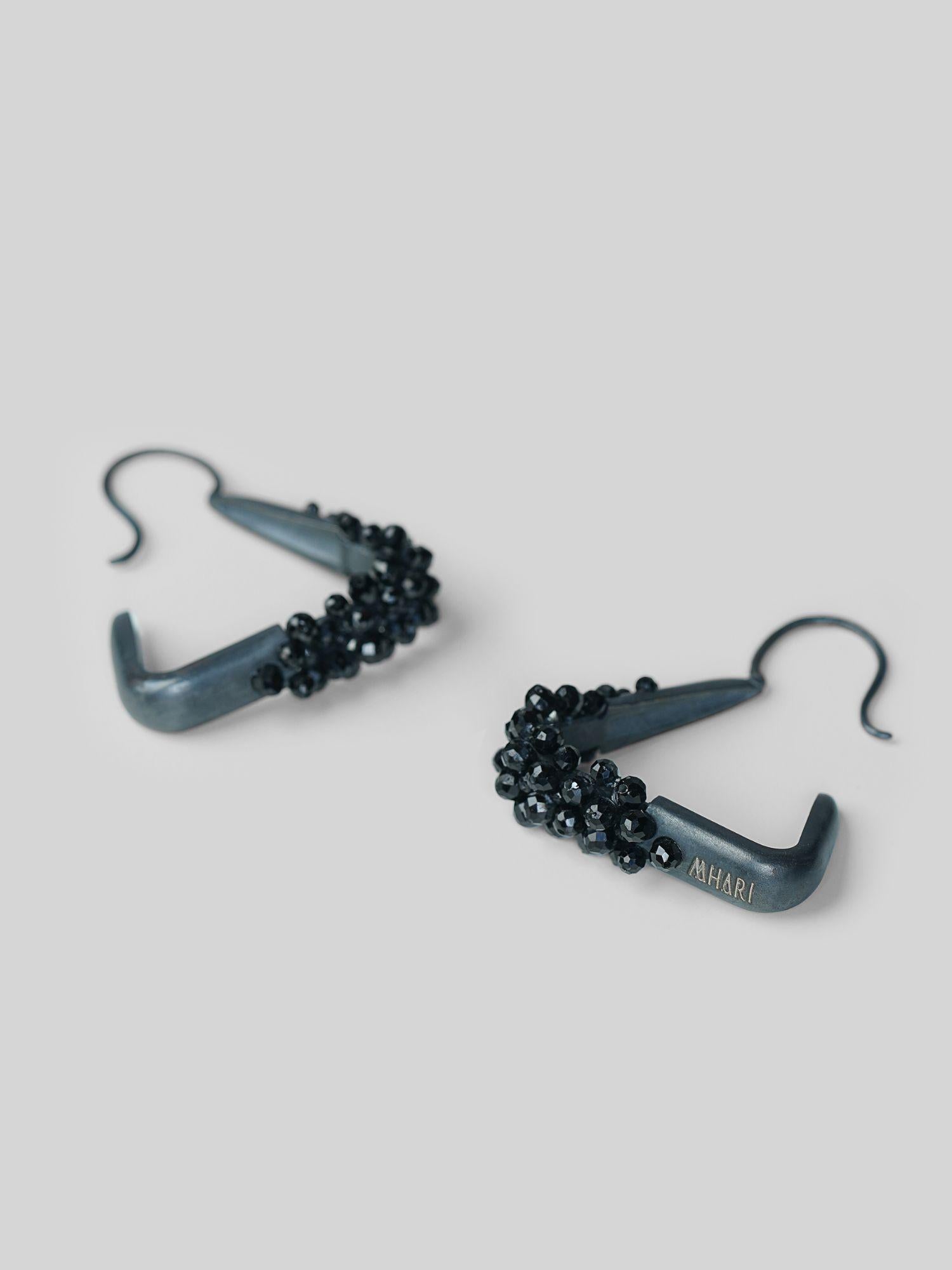 Angled product shot of Maré spinel hanger earrings in black rhodium showing triangular silhouette and bead detail.