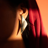Mosaic mother of pearl drop earrings in dramatic warm editorial lighting against a red backdrop.