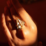 Mosaic mother of pearl cocktail ring held in warm golden light, full sculptural form visible.