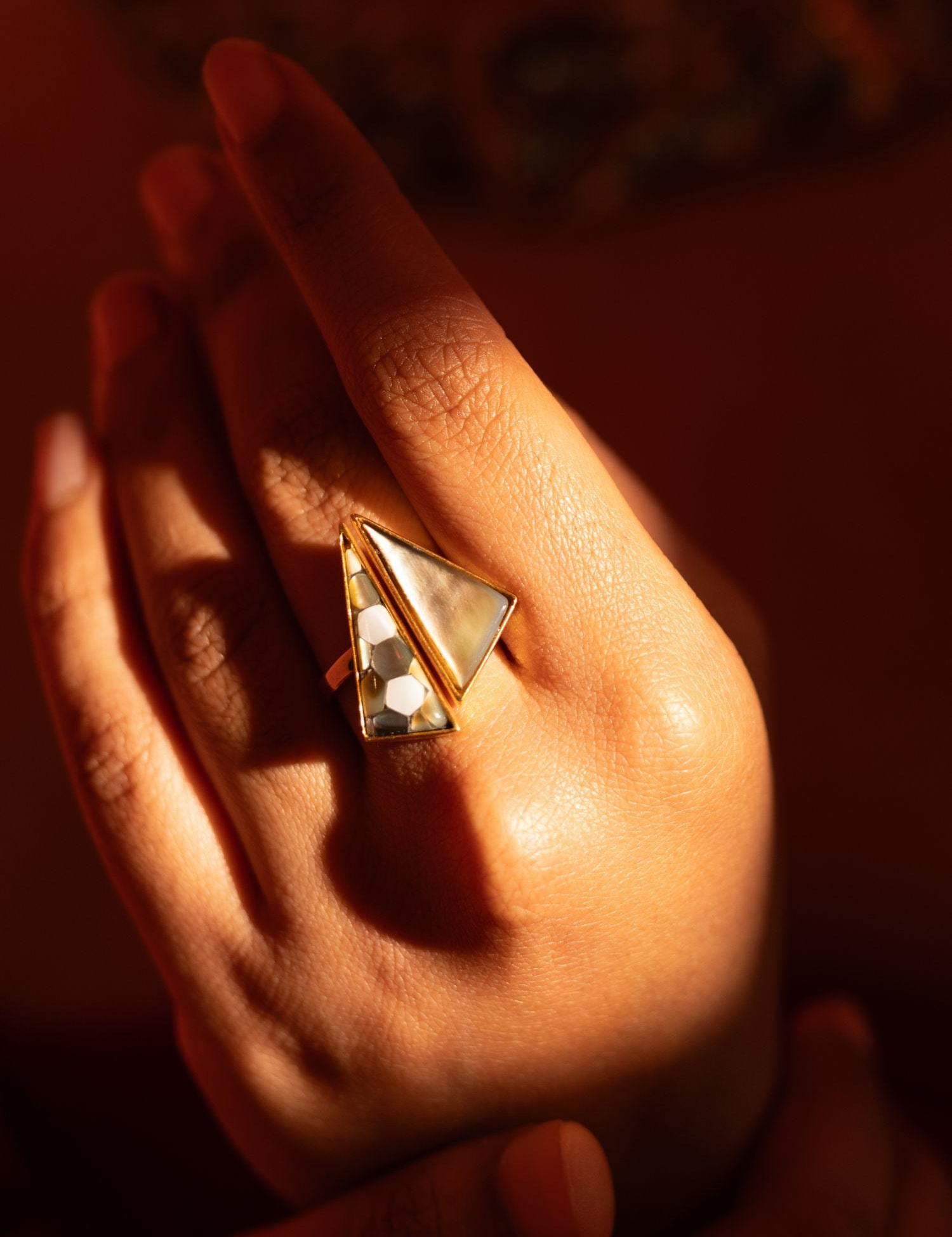 Mosaic mother of pearl cocktail ring held in warm golden light, full sculptural form visible.