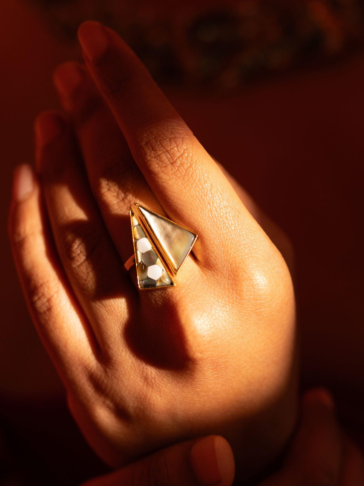 Mosaic mother of pearl cocktail ring held in warm golden light, full sculptural form visible.