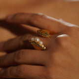 Close-up of Noira natural pearl ring and zircon ring worn together on hand in warm golden light.