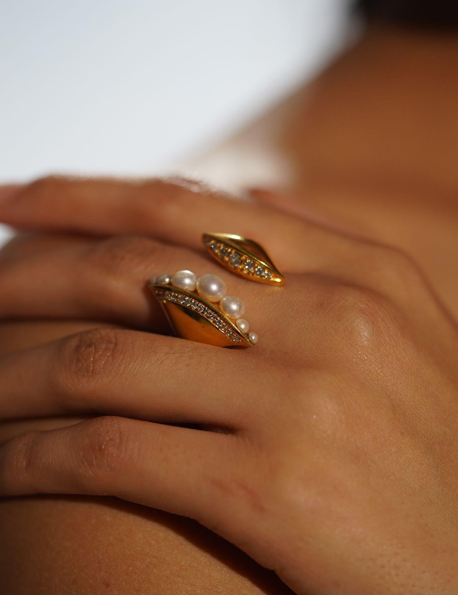 Noira pearl cocktail ring with zircon band on model's hand in warm editorial light.