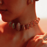 Opal Perspective statement necklace worn in a soft portrait, model's hand resting at collarbone.
