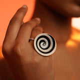 Orbis black enamel cocktail ring in white rhodium worn on hand in dramatic warm editorial light.