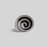 Orbis cocktail ring with spiral black enamel and zircon detail in white rhodium, front angle on neutral background.