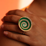 Orbis green enamel cocktail ring worn on hand resting on shoulder in warm orange editorial light.