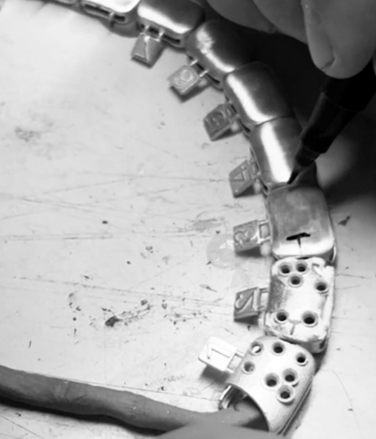 Artisan setting stones into silver jewellery piece using precision tool, black and white