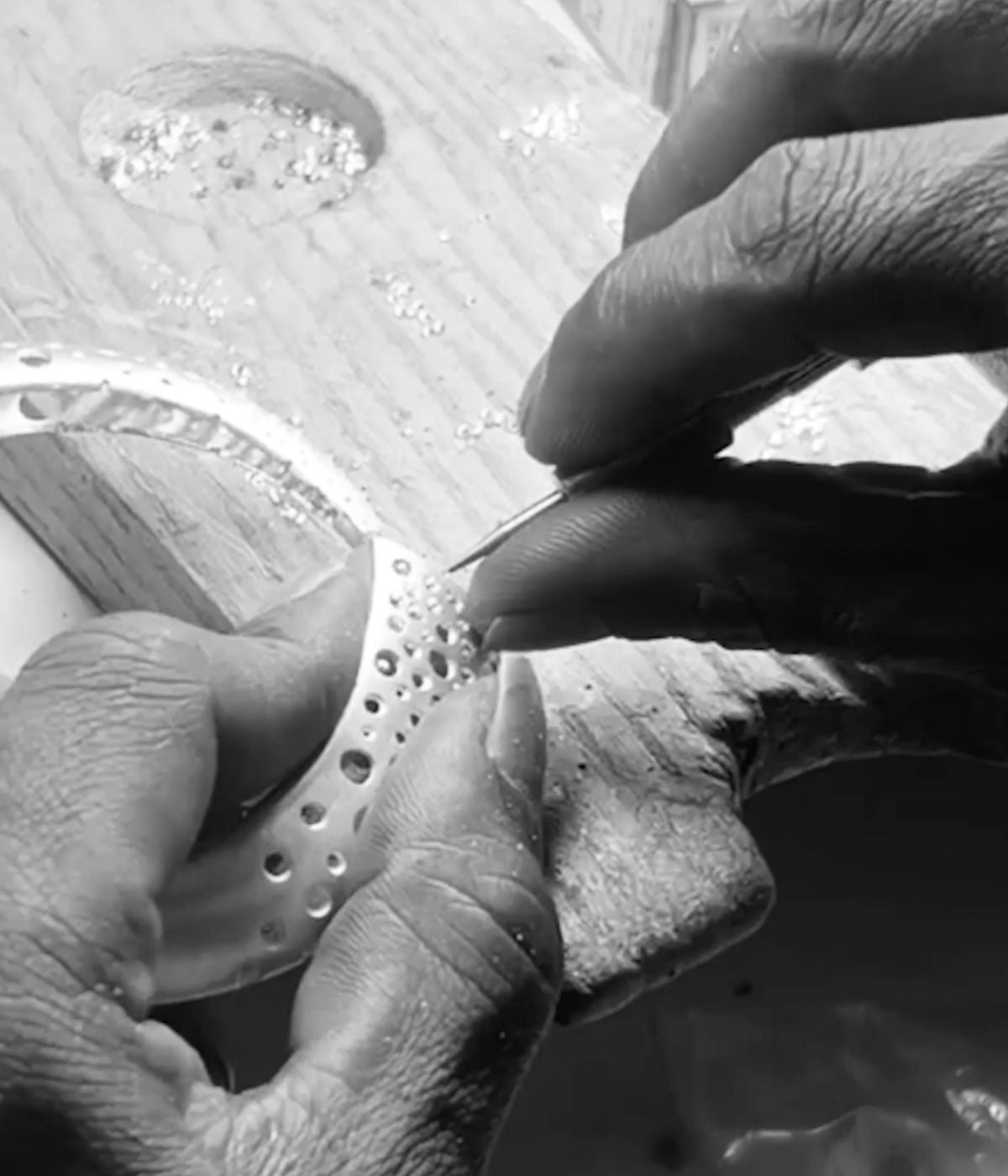 Close-up of hands setting small stones into silver jewellery, black and white