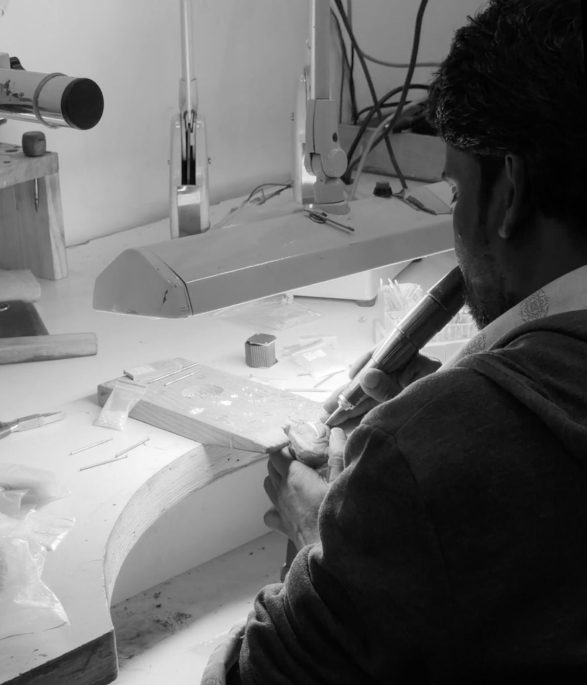 Jewellery maker working at studio bench on silver piece, black and white