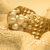 Close-up of gold open cuff with natural pearl cluster setting on white surface