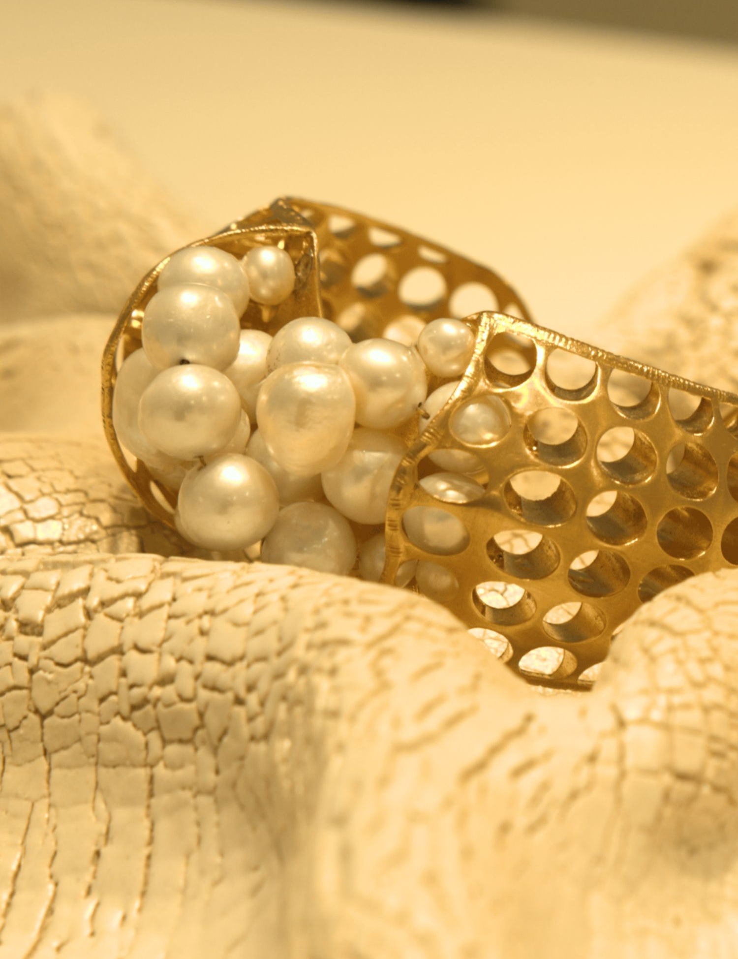 Close-up of gold open cuff with natural pearl cluster setting on white surface