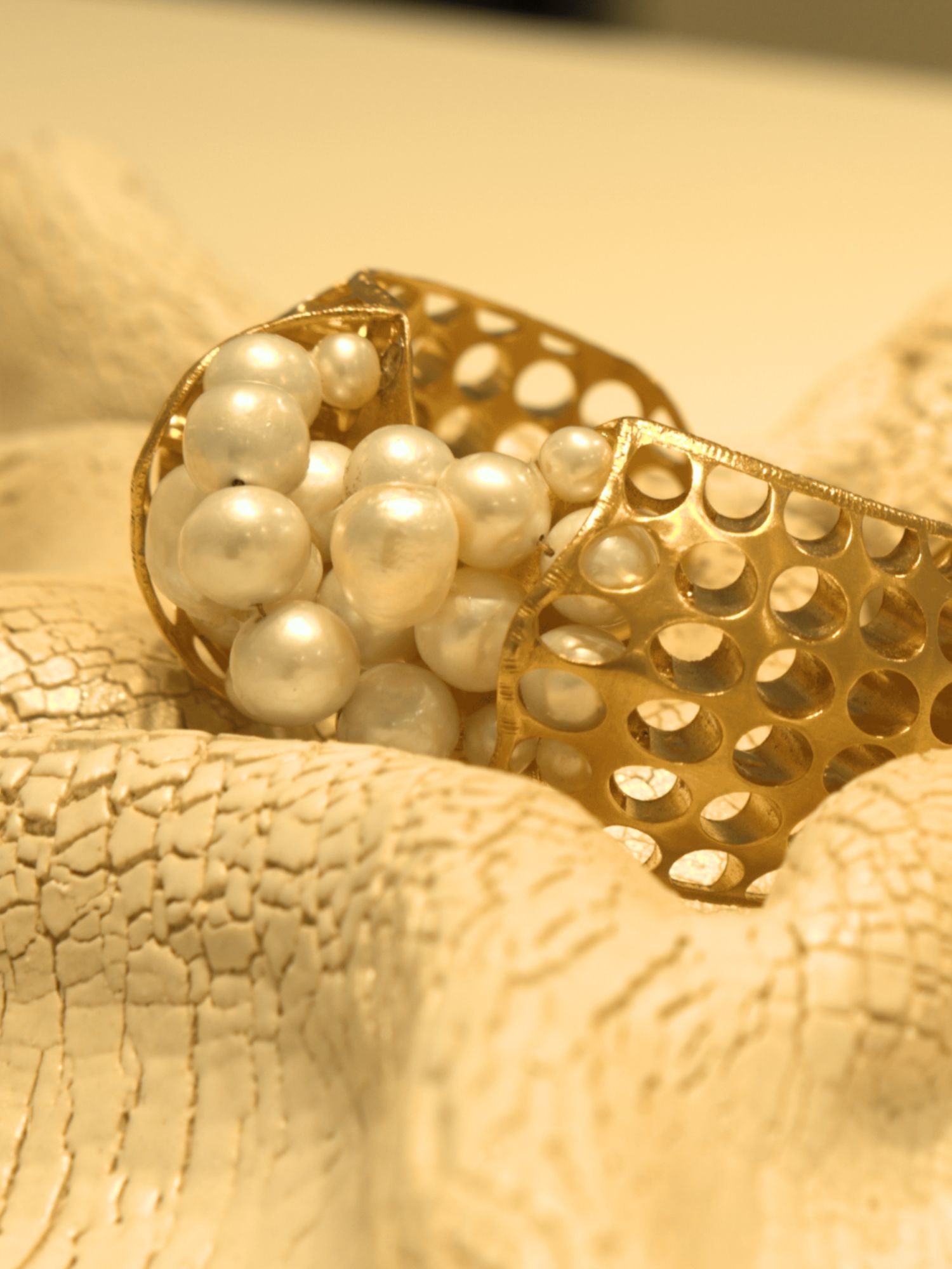 Close-up of gold open cuff with natural pearl cluster setting on white surface