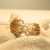 Open gold cuff bracelet set with natural pearls on white textured surface