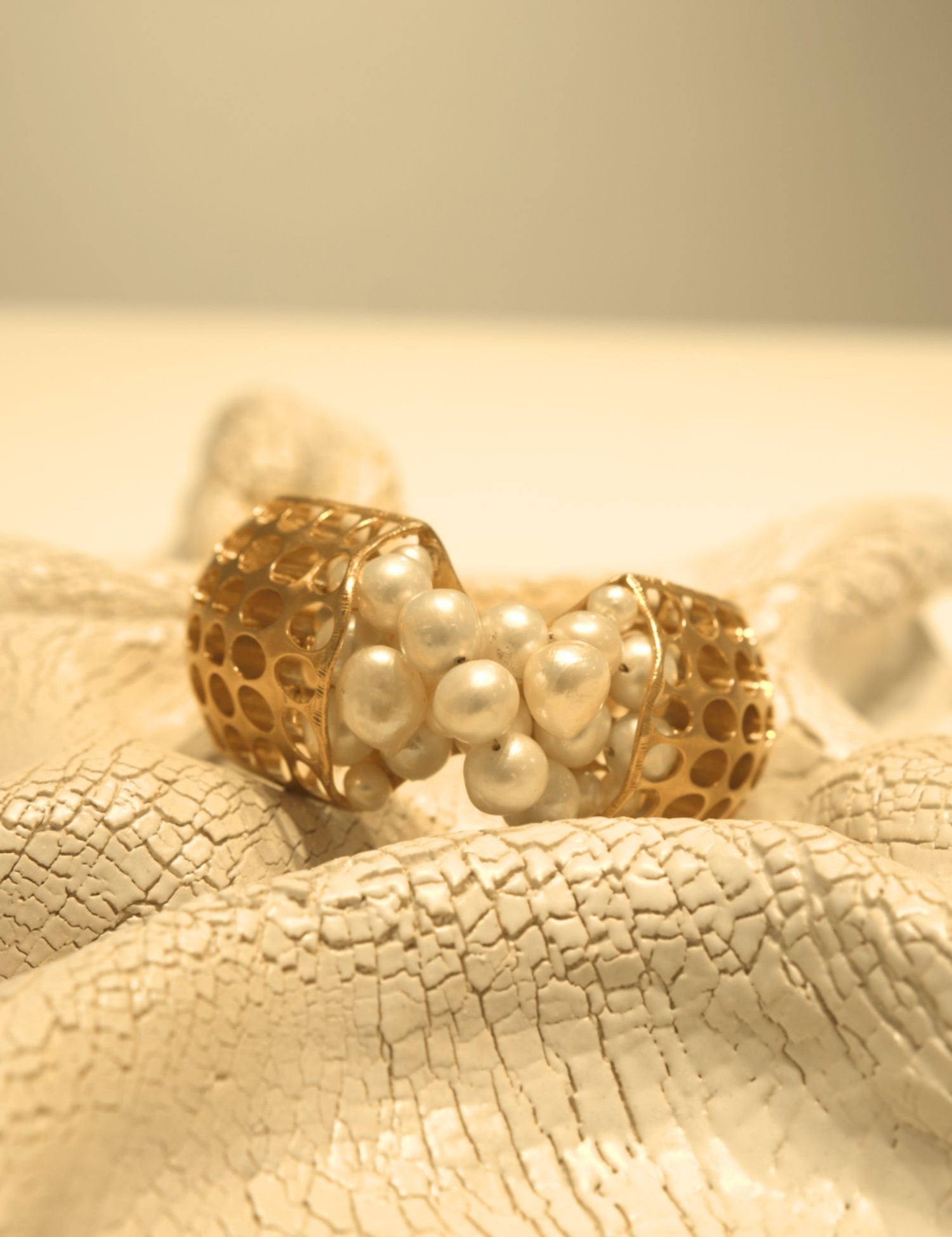 Open gold cuff bracelet set with natural pearls on white textured surface