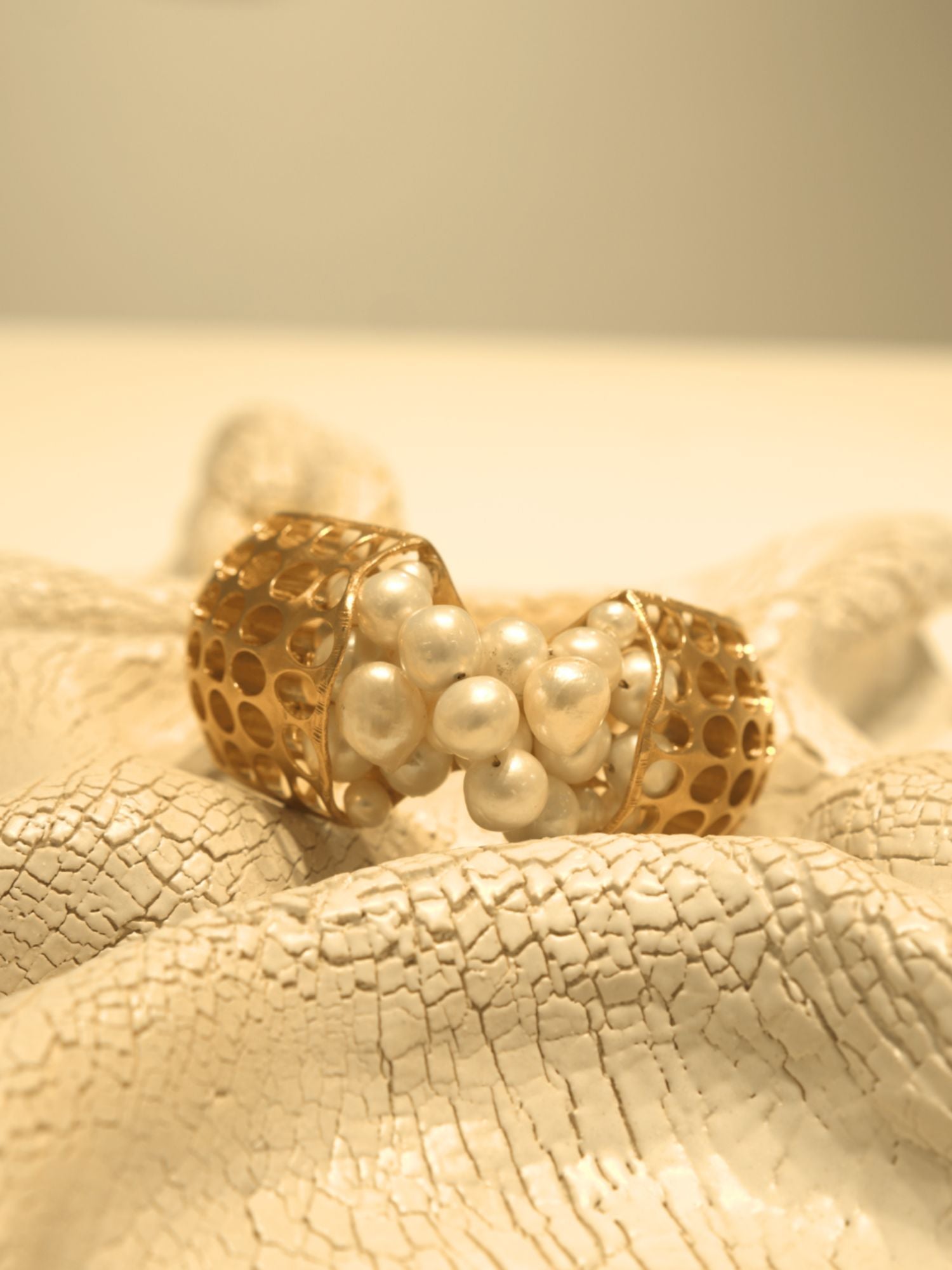 Open gold cuff bracelet set with natural pearls on white textured surface