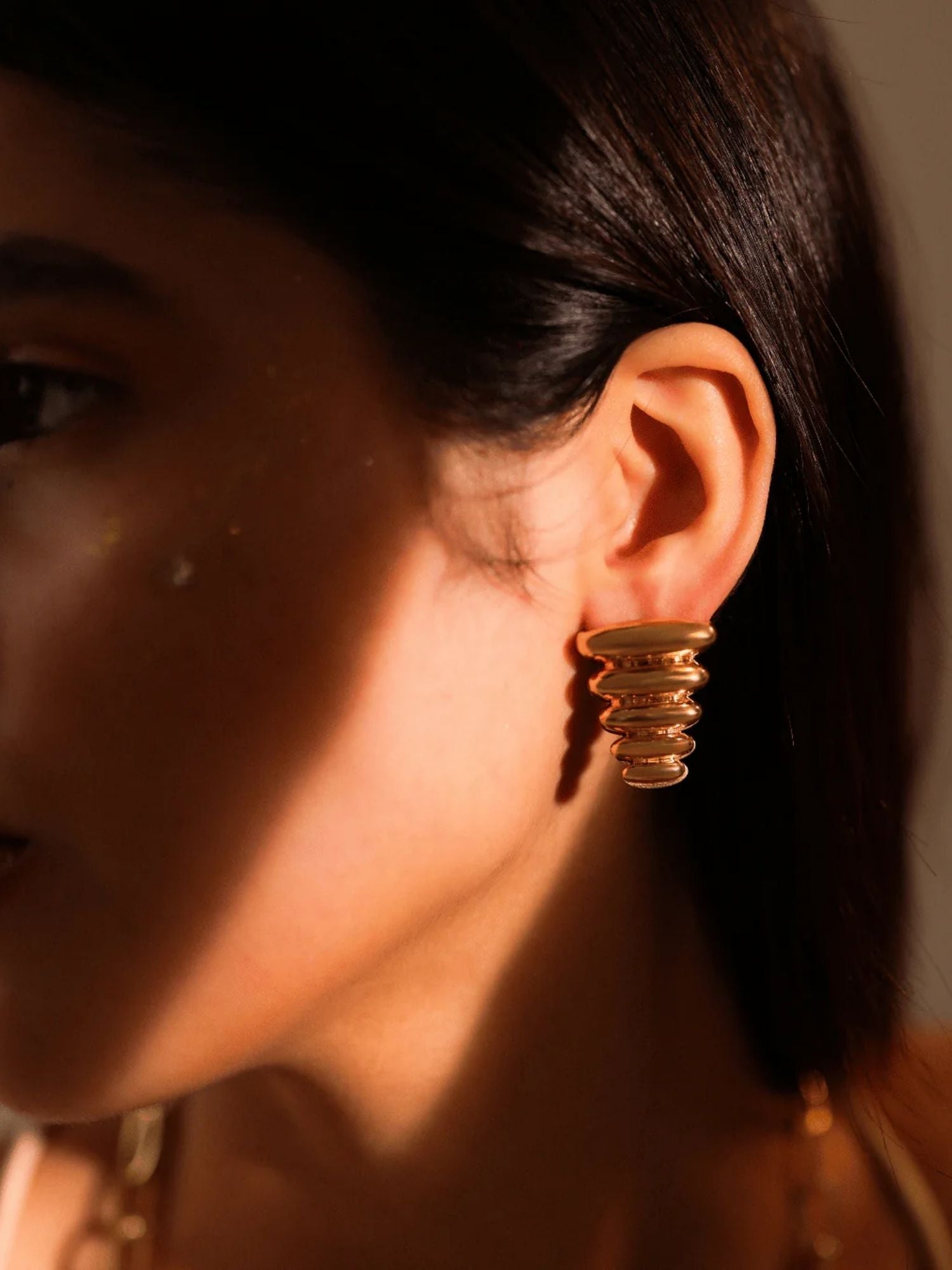 Close-up of gold ribbed triangle pebble earring on model's ear
