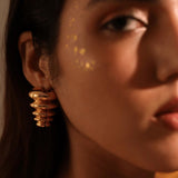Model wearing sculptural gold triangle pebble earrings, face forward in warm light