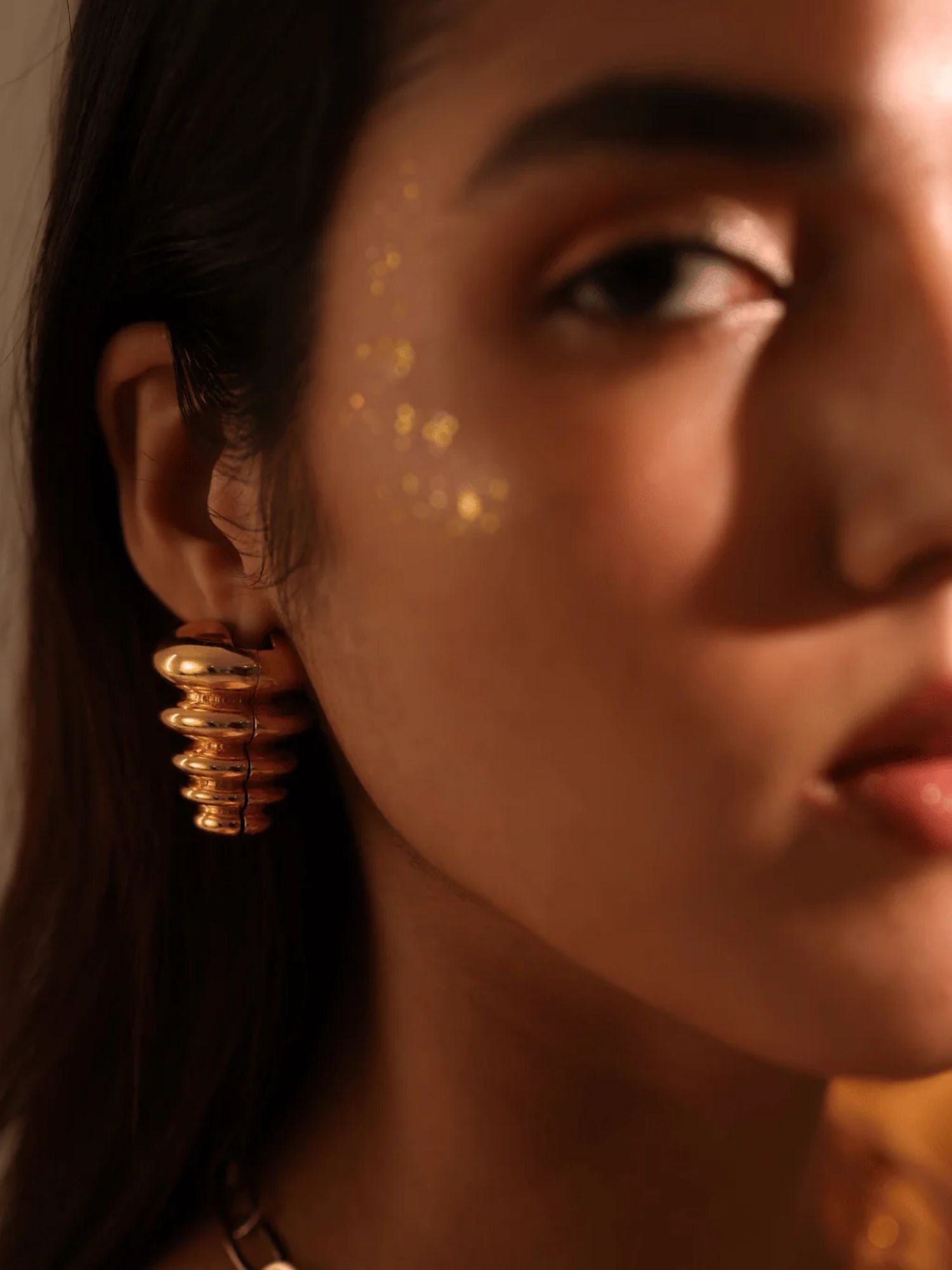 Model wearing sculptural gold triangle pebble earrings, face forward in warm light