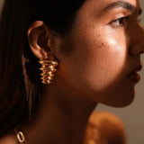 Side profile of model wearing gold triangle pebble earring in warm golden light