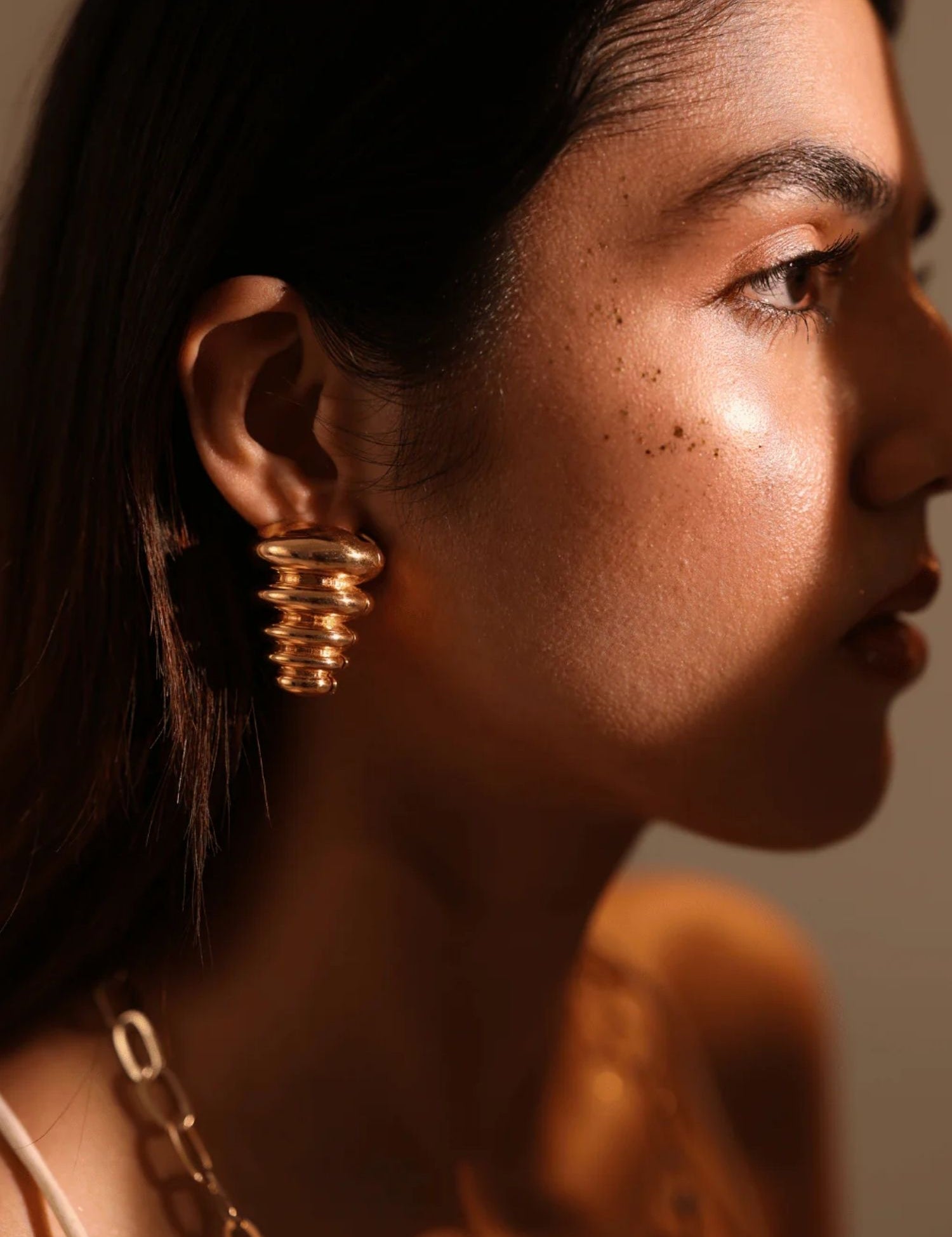 Side profile of model wearing gold triangle pebble earring in warm golden light