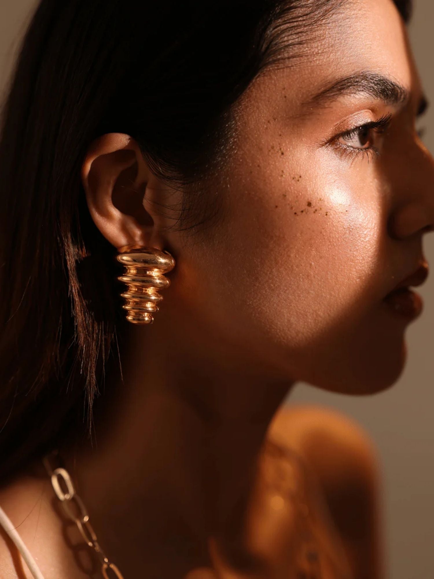 Side profile of model wearing gold triangle pebble earring in warm golden light