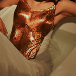 Model wearing handcrafted copper corset with CZ accents, reclining in white backdrop