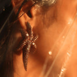 Model wearing gold starfish earring, light flare across hair and shoulder
