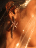 Model wearing gold starfish earring, light flare across hair and shoulder