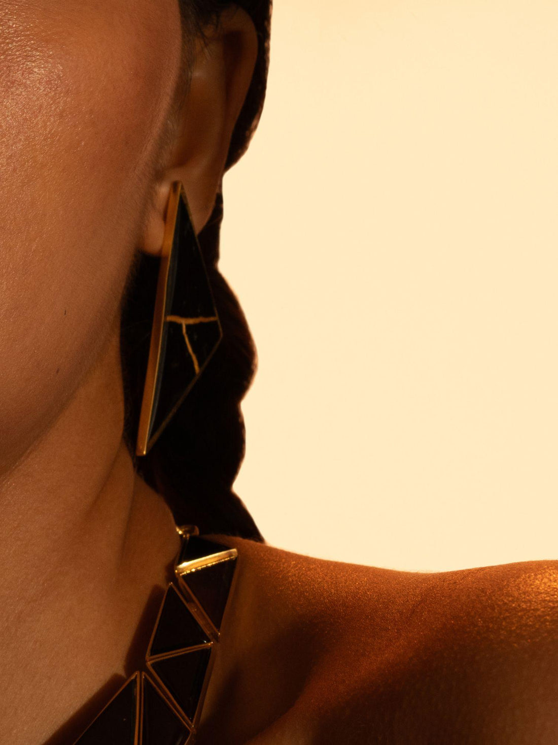 Tsugumi kintsugi triangular drop earrings with black enamel and gold crack detail on neutral background.