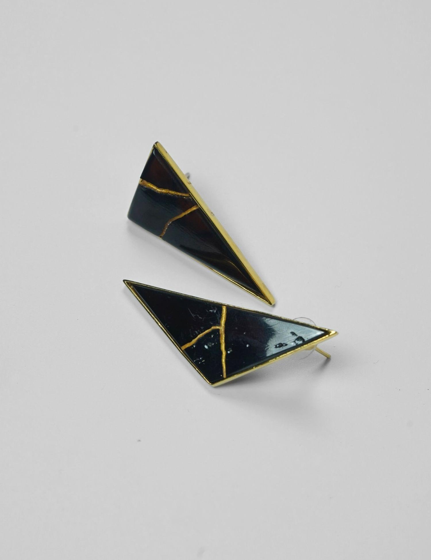 Tsugumi kintsugi triangular drop earrings with black enamel and gold crack detail on neutral background.