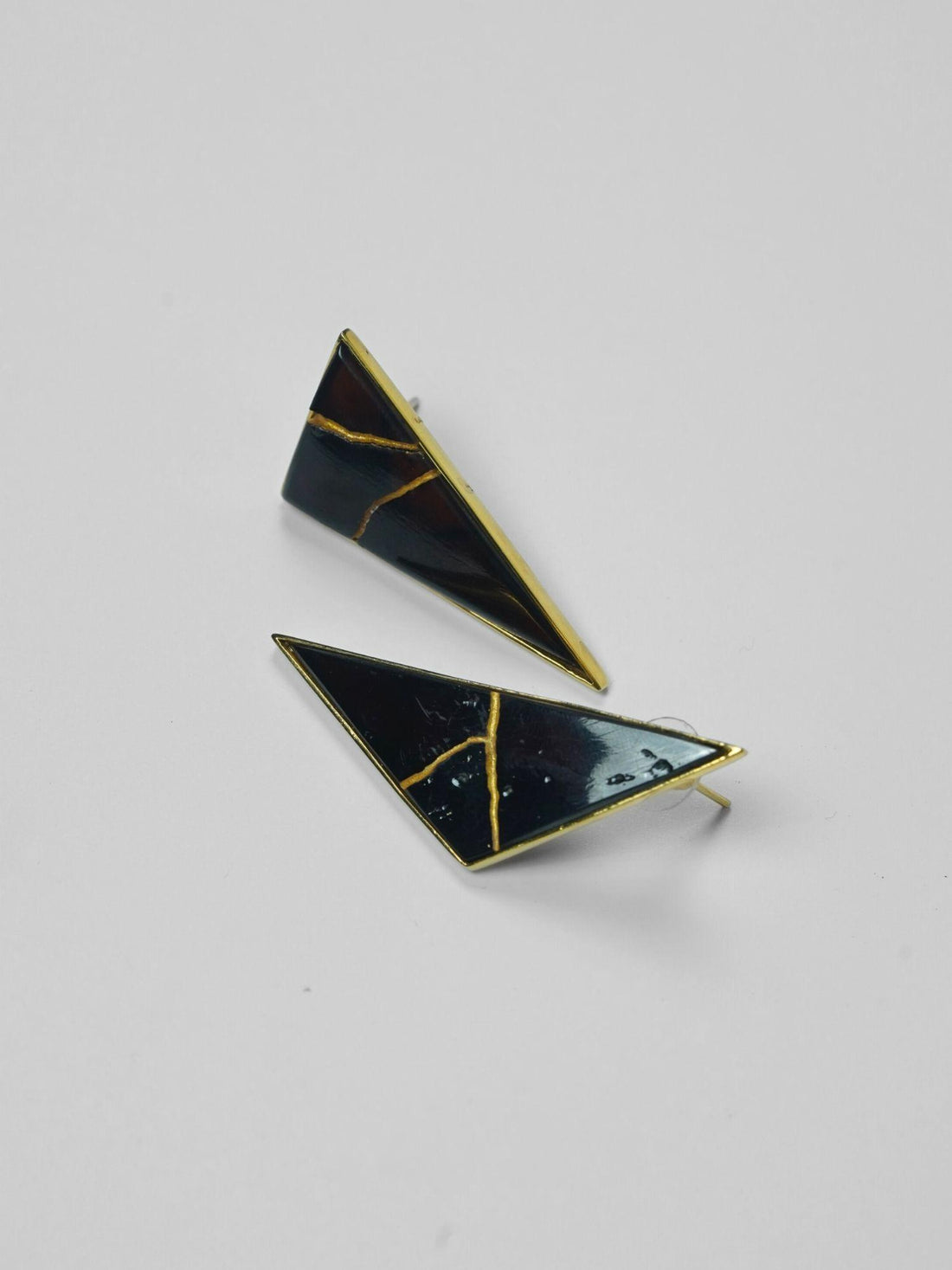 Tsugumi kintsugi triangular drop earrings with black enamel and gold crack detail on neutral background.