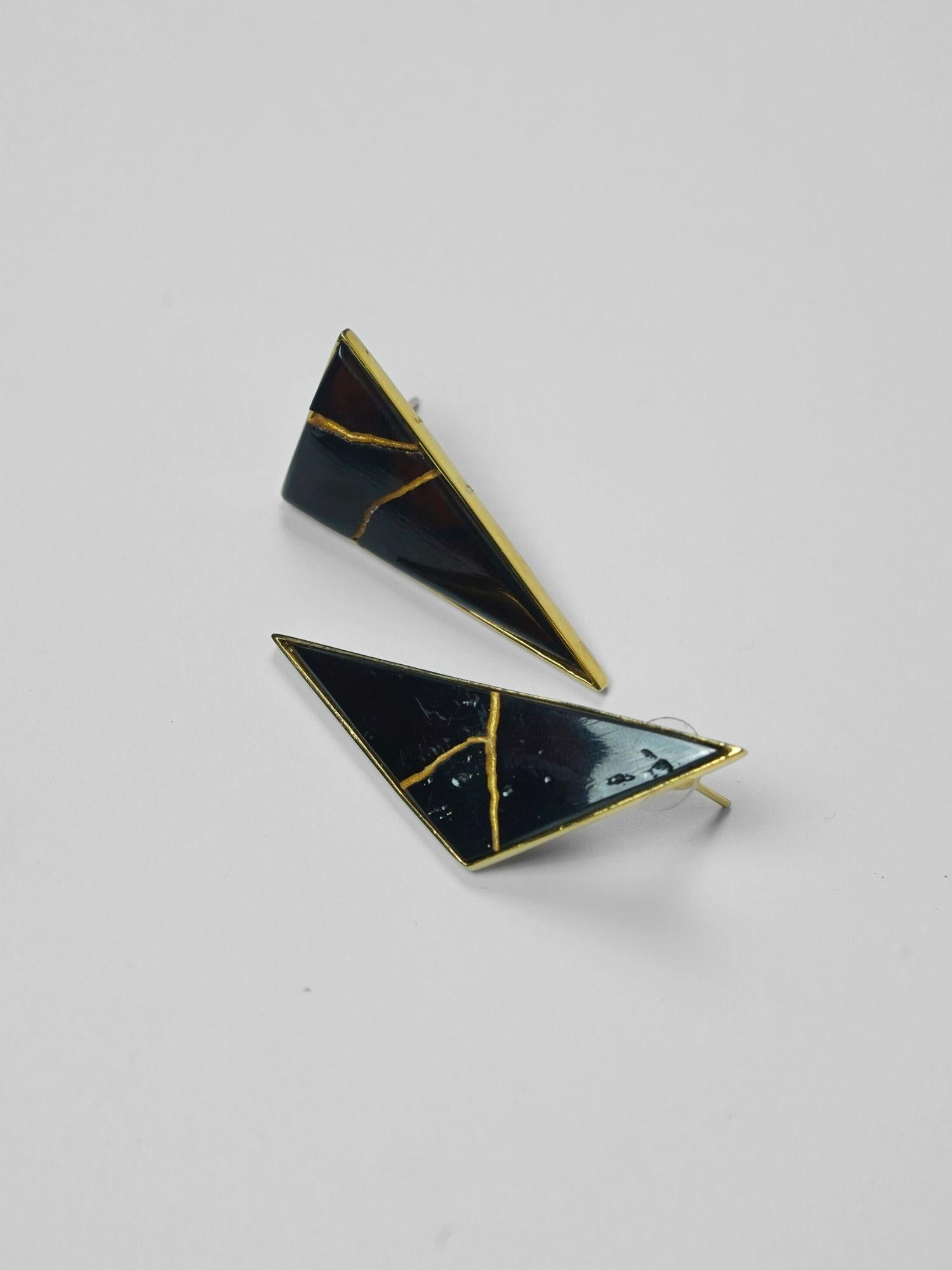 Tsugumi kintsugi triangular drop earrings with black enamel and gold crack detail on neutral background.
