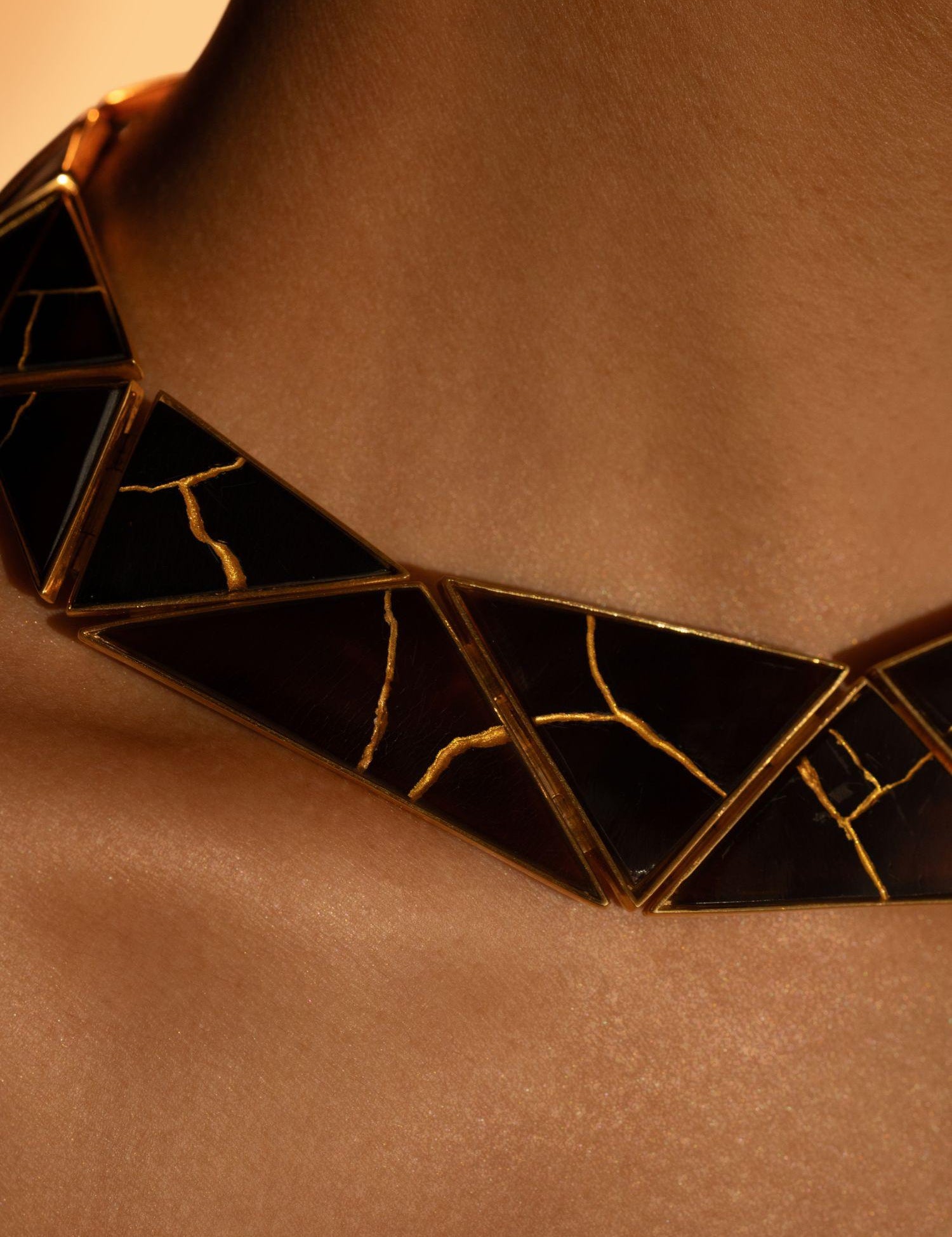 Tsugumi kintsugi statement necklace worn close to décolletage showing gold crack detail on black panels.