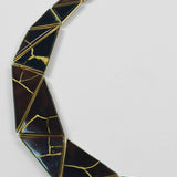 Tsugumi necklace crescent form close-up showing black enamel and gold kintsugi line detail on neutral background.