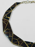Tsugumi necklace crescent form close-up showing black enamel and gold kintsugi line detail on neutral background.