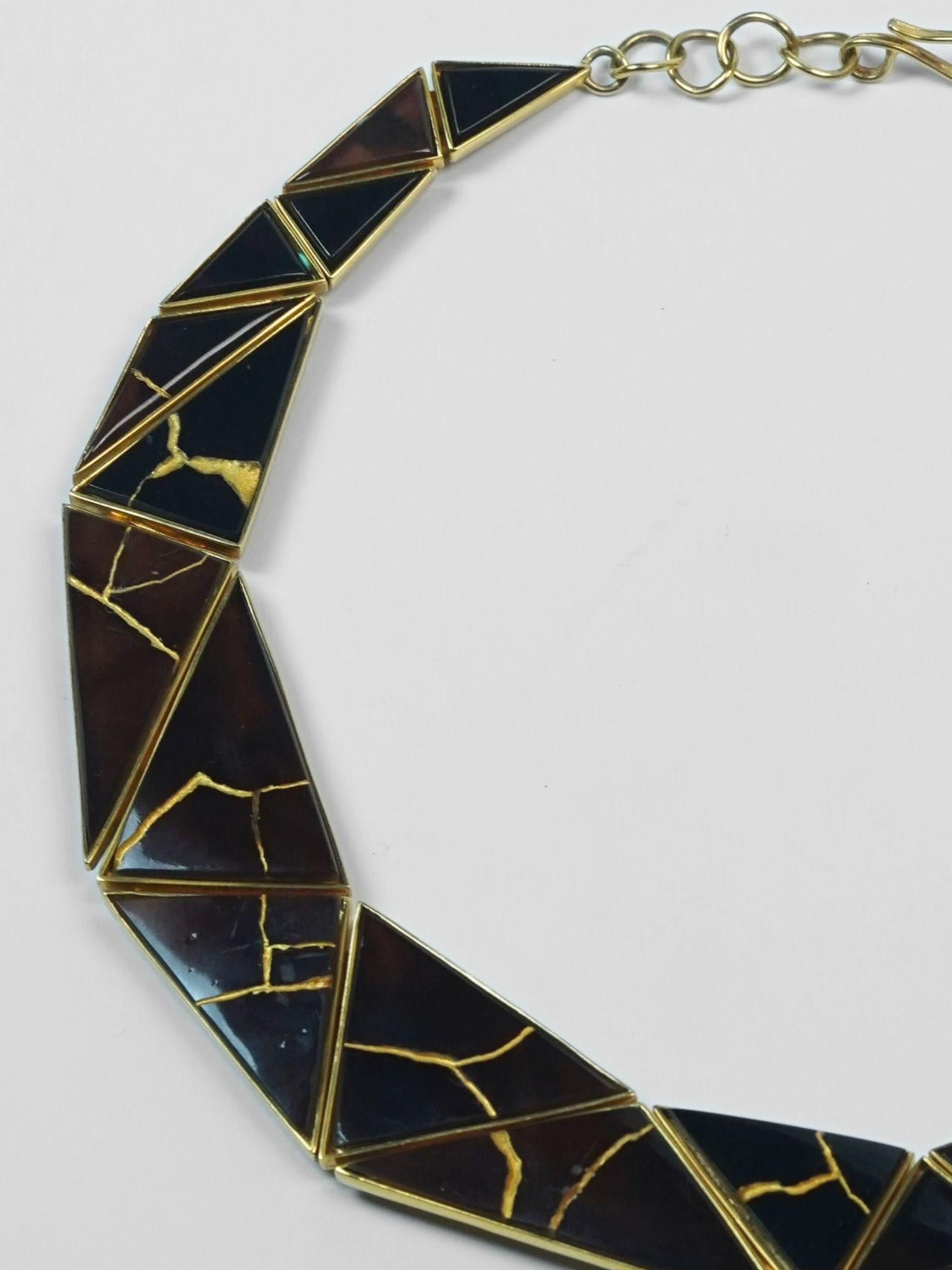 Tsugumi necklace crescent form close-up showing black enamel and gold kintsugi line detail on neutral background.