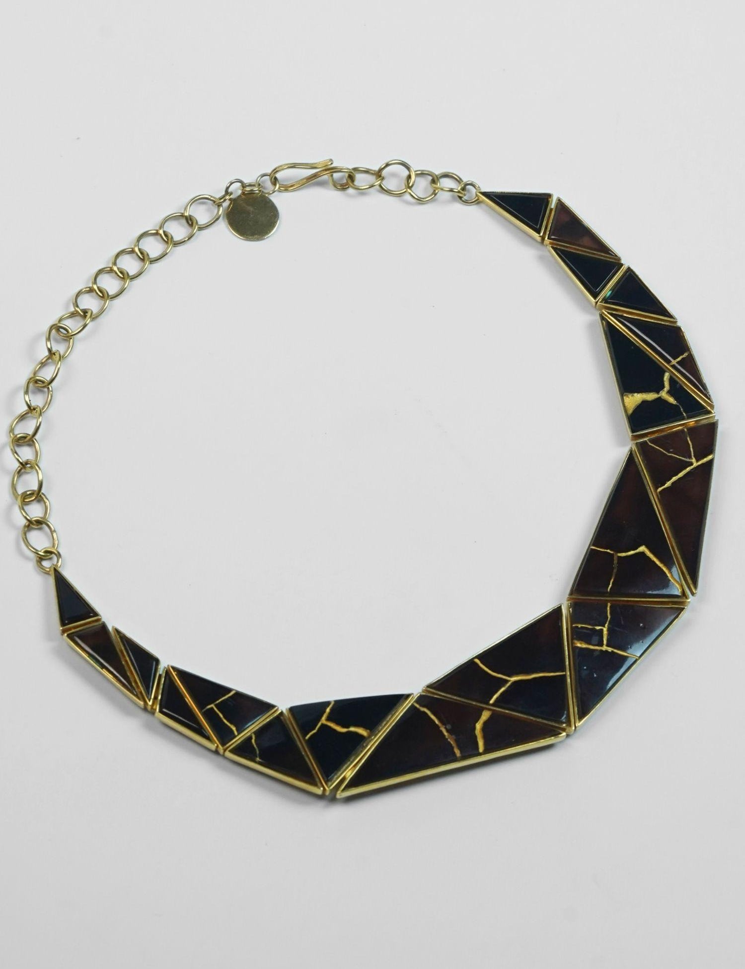 Tsugumi kintsugi necklace with black enamel panels and gold crack detail, full length with chain on neutral background.
