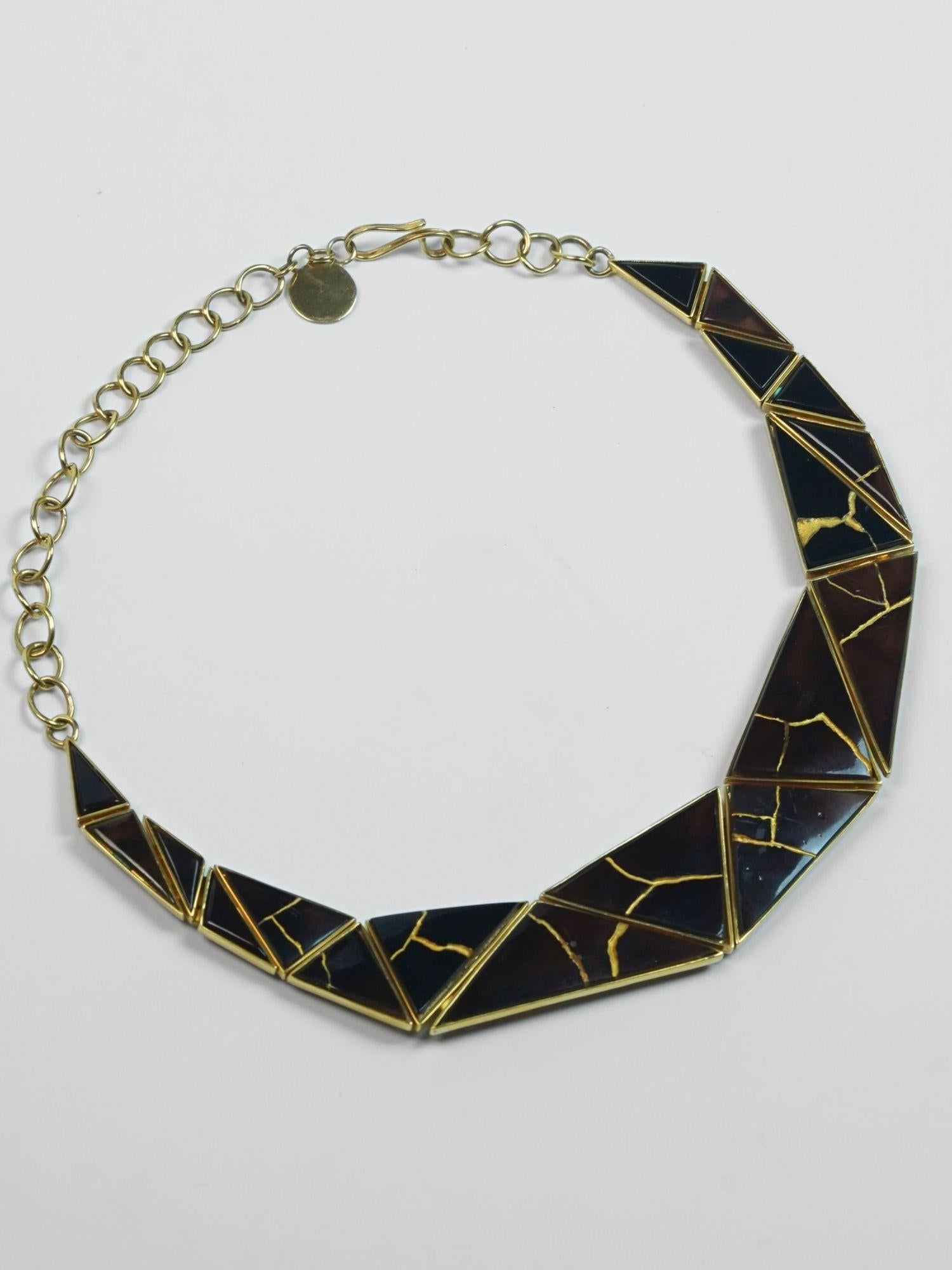 Tsugumi kintsugi necklace with black enamel panels and gold crack detail, full length with chain on neutral background.