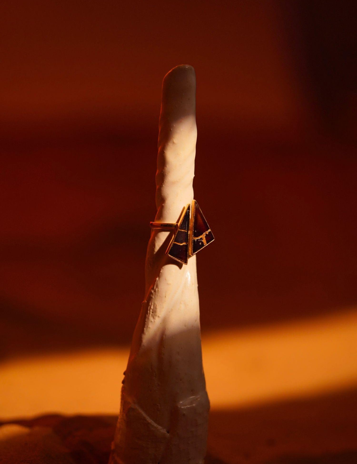 Tsugumi kintsugi cocktail ring with black enamel and gold crack lines in warm directional light.