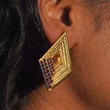 Vélora blue CZ geometric diamond statement earring in gold worn close to ear in profile shot.