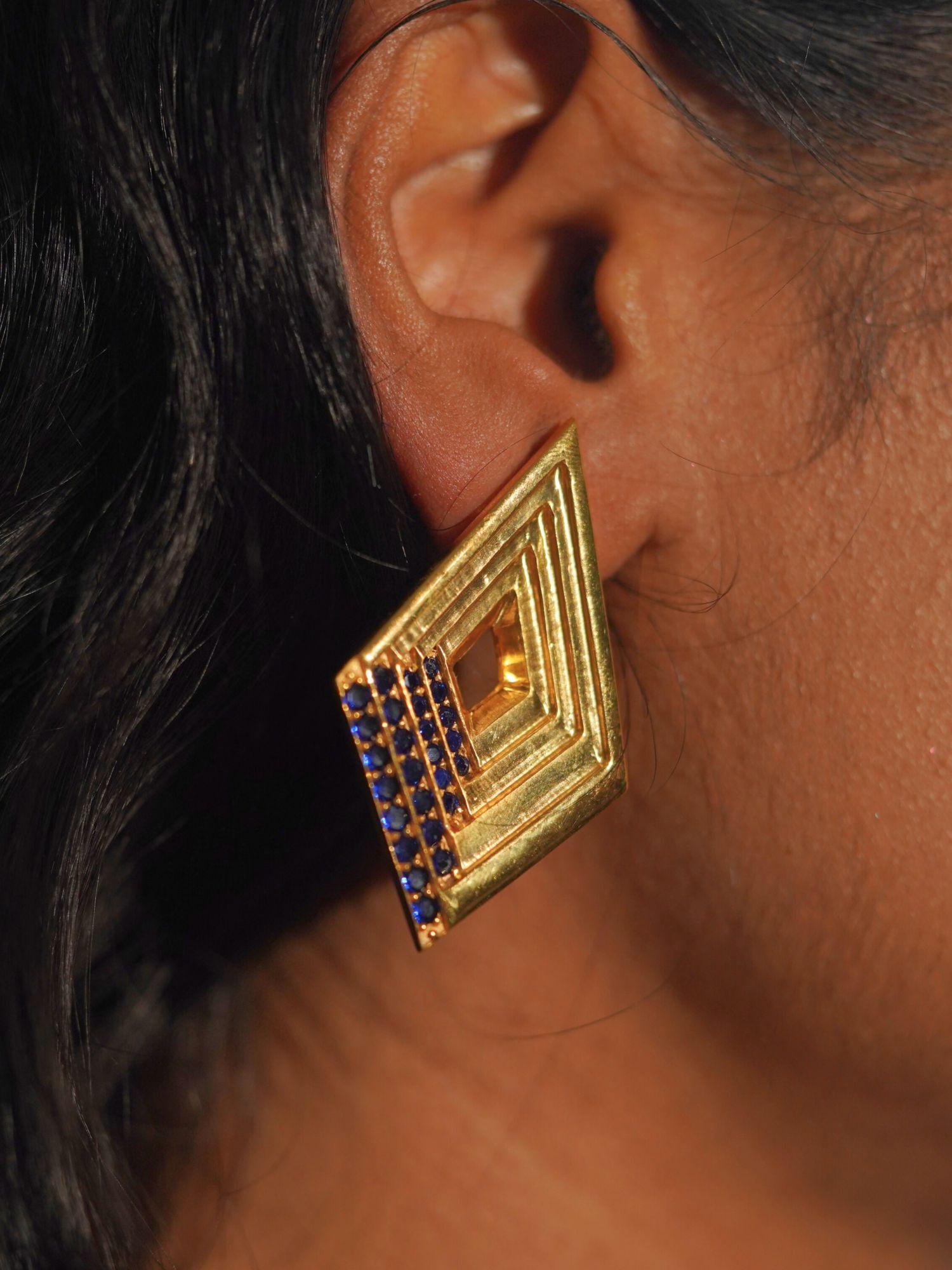 Vélora blue CZ geometric diamond statement earring in gold worn close to ear in profile shot.