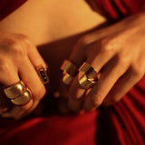 Dramatic close-up of gold dome curve ring on model's hand against red backdrop