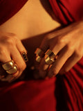 Dramatic close-up of gold dome curve ring on model's hand against red backdrop