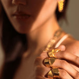Close-up of model's fingers wearing sculptural gold ribbon ring in warm light